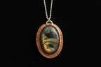 A handmade oval pendant necklace featuring a polished labradorite stone with a blue and gold sheen, set in a copper-toned bezel with a silver-toned chain against a solid black background.