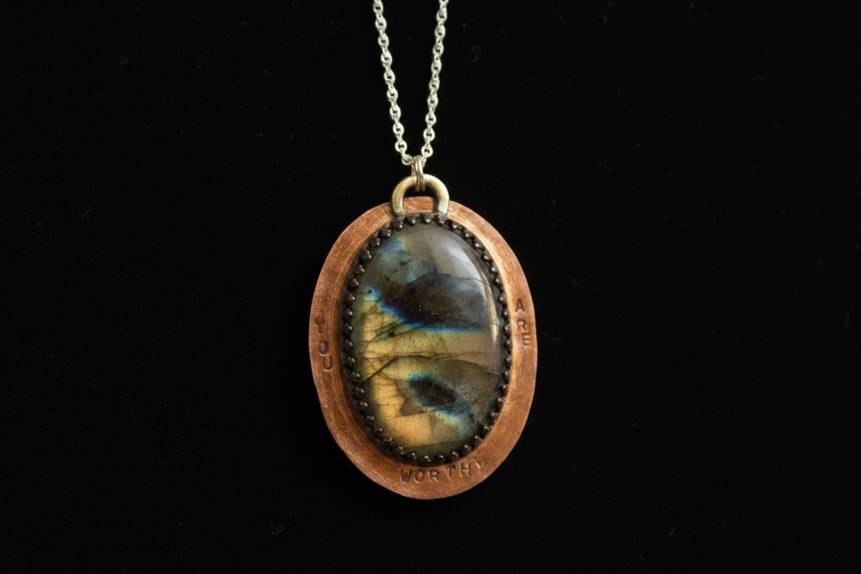 A handmade oval pendant necklace featuring a polished labradorite stone with a blue and gold sheen, set in a copper-toned bezel with a silver-toned chain against a solid black background.