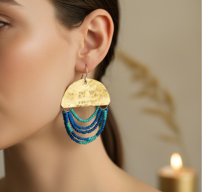 Gold earring with blue beads worn by a person, blurred background