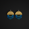 A pair of handmade dangle earrings on a solid black background. Each earring features a hammered gold-tone semicircle disc engraved with 'YOU ARE ENOUGH' and 'I AM ENOUGH', with three curved strands of small beads in shades of blue, teal, and turquoise hanging below.