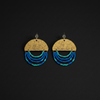 A pair of handmade dangle earrings on a solid black background. Each earring features a hammered gold-tone semicircle disc engraved with 'YOU ARE ENOUGH' and 'I AM ENOUGH', with three curved strands of small beads in shades of blue, teal, and turquoise hanging below.