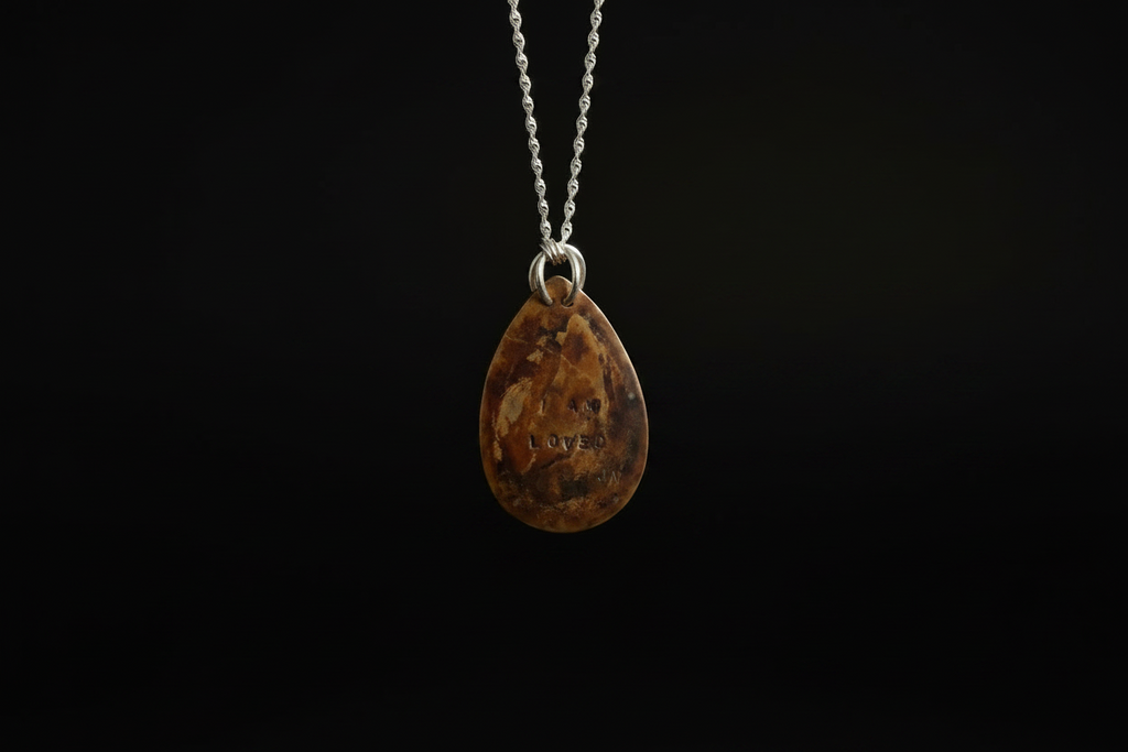 A teardrop-shaped brown gemstone pendant with natural inclusions, suspended from a silver chain against a solid black background.