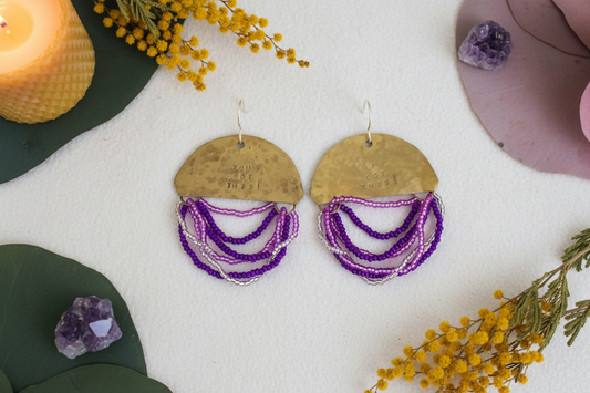 Half Moon Wordkeeper Earrings Got This by Jewellery by JN, hammered brass crescents with purple, lilac, and silver bead fringe and handmade sterling silver ear wires, shown front-facing.
